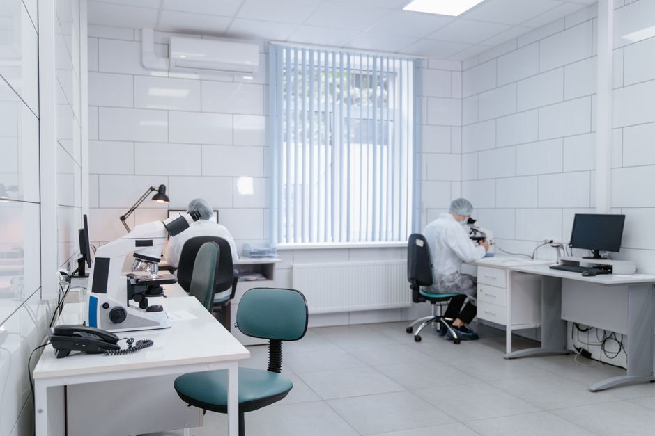 Clean, modern laboratory interior with microscopes and researchers in protective gear conducting analysis.